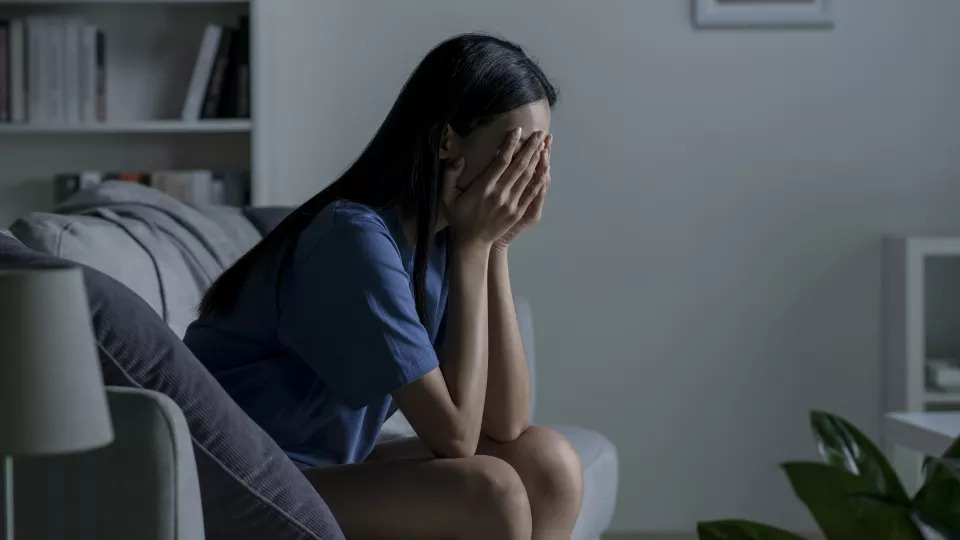 Young woman sitting on couch with head in hands